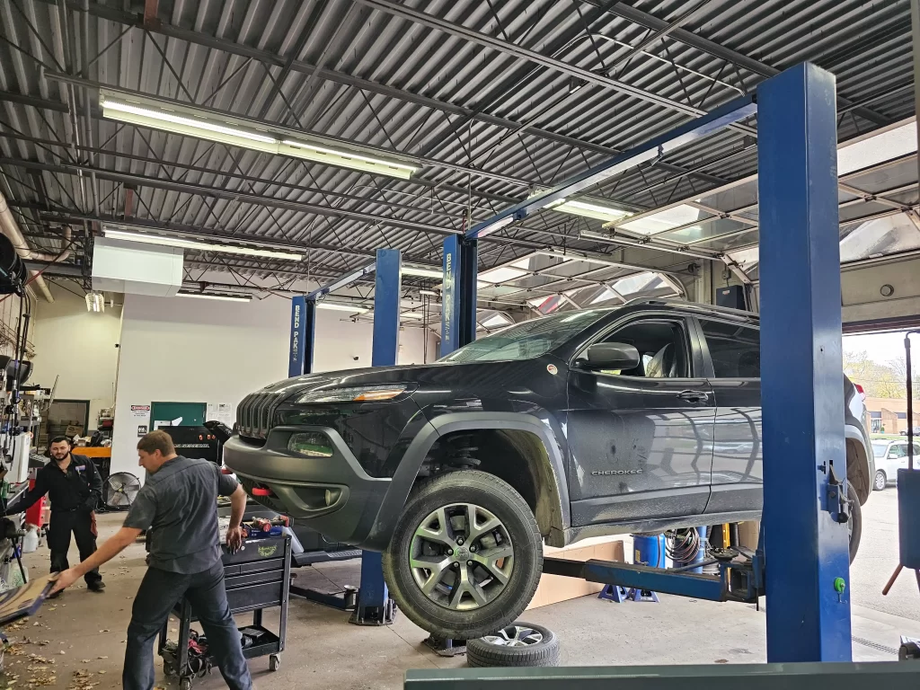 A black Jeep Cherokee on a lift being serviced by mechanics in a busy bay at Real Pro Auto.