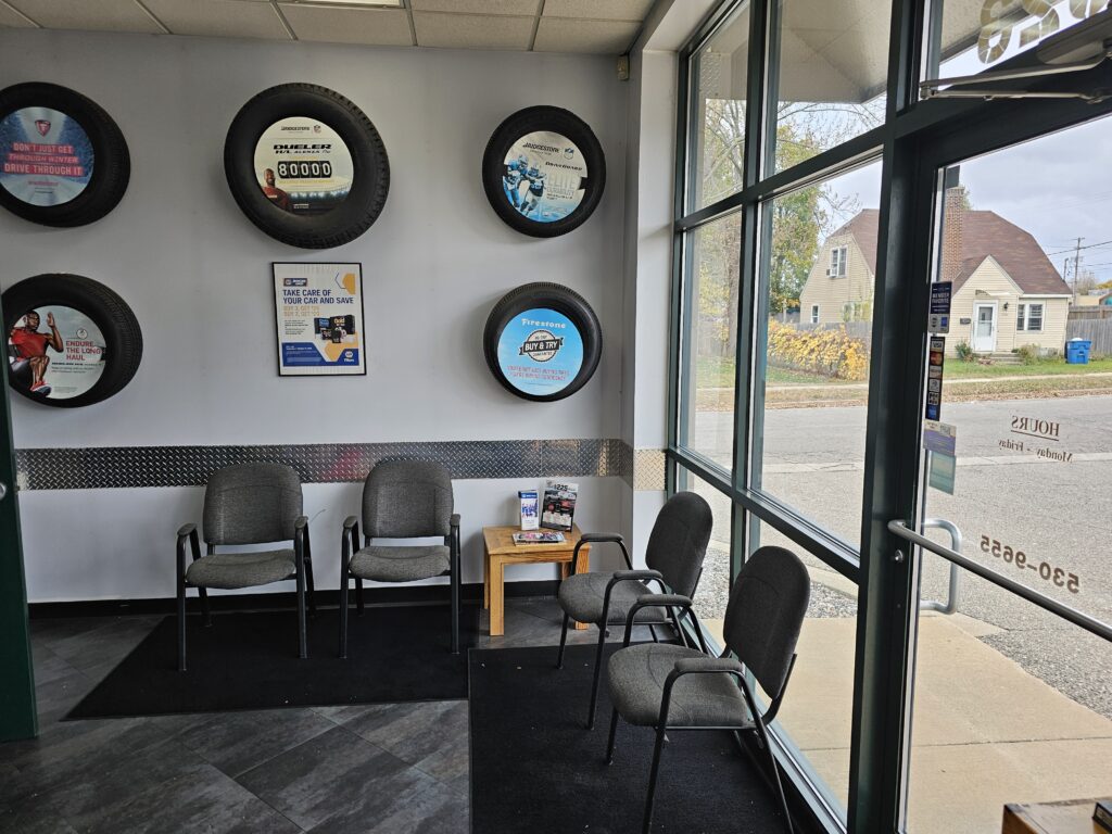 Waiting area with chairs, a small table, wall-mounted tire displays, and large glass windows.