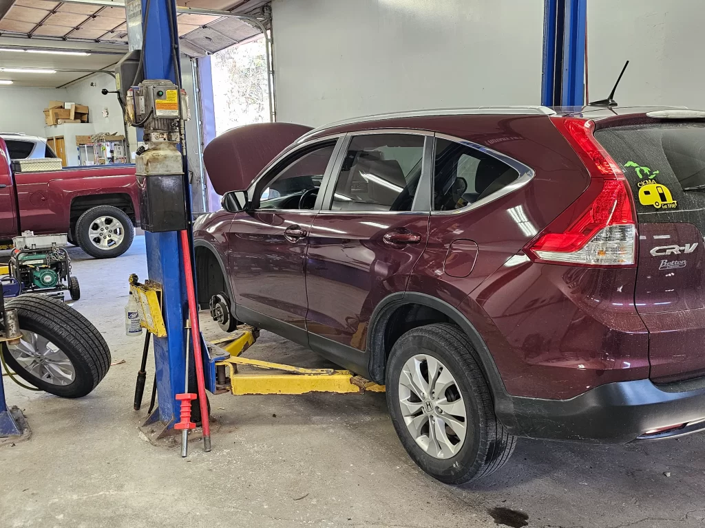 A maroon Honda CR-V on a lift in an auto repair shop with its hood open for maintenance.