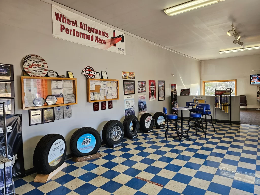 Real Pro Auto waiting area with checkered floor, tires on display, awards, and a "Wheel Alignments" banner.