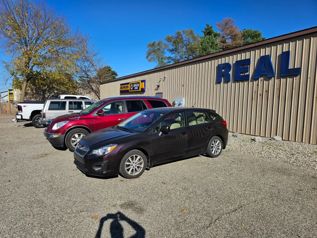 Parked cars outside Real Pro Auto with a "NAPA AutoCare Center" sign on a sunny day.