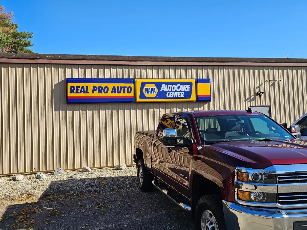 Real Pro Auto NAPA AutoCare Center sign on a building with a parked maroon pickup truck in front.