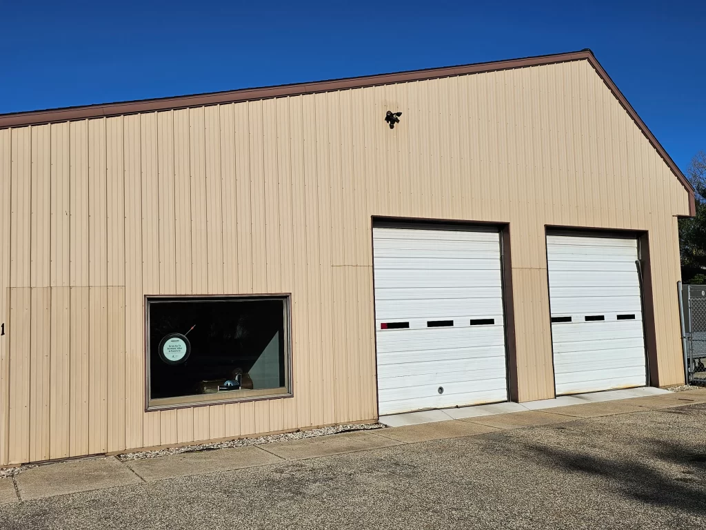 Beige building with two white garage doors, a single window, and a shadow on the pavement.