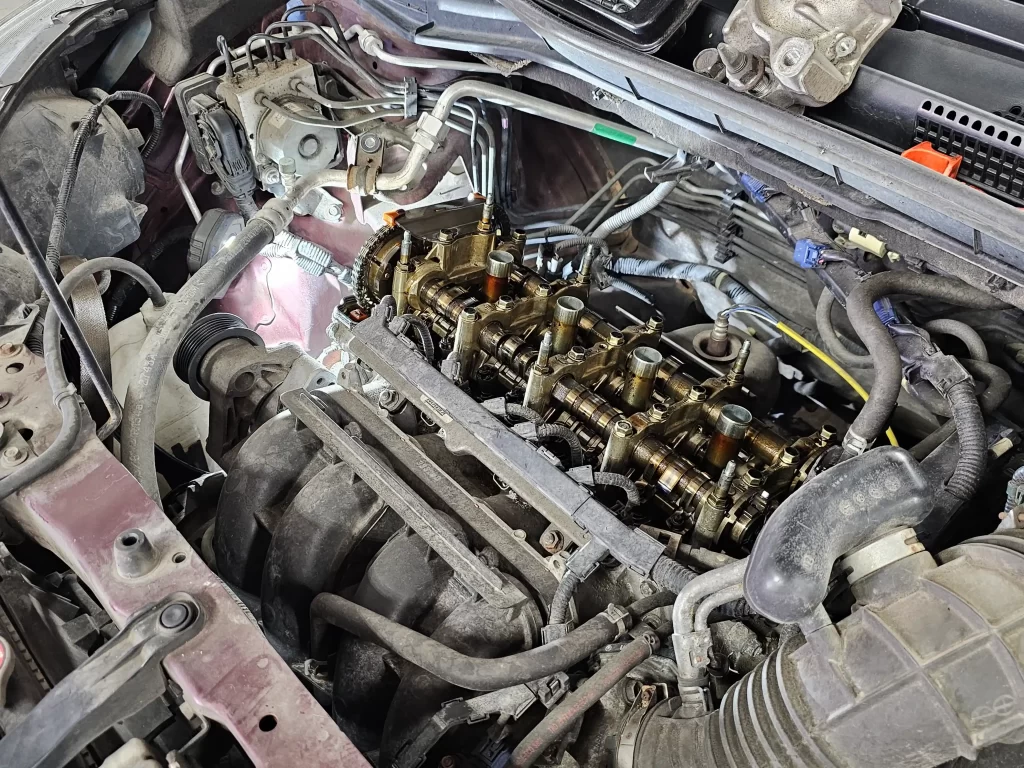 Close-up of an open car engine undergoing repairs, showing exposed camshaft and surrounding components.