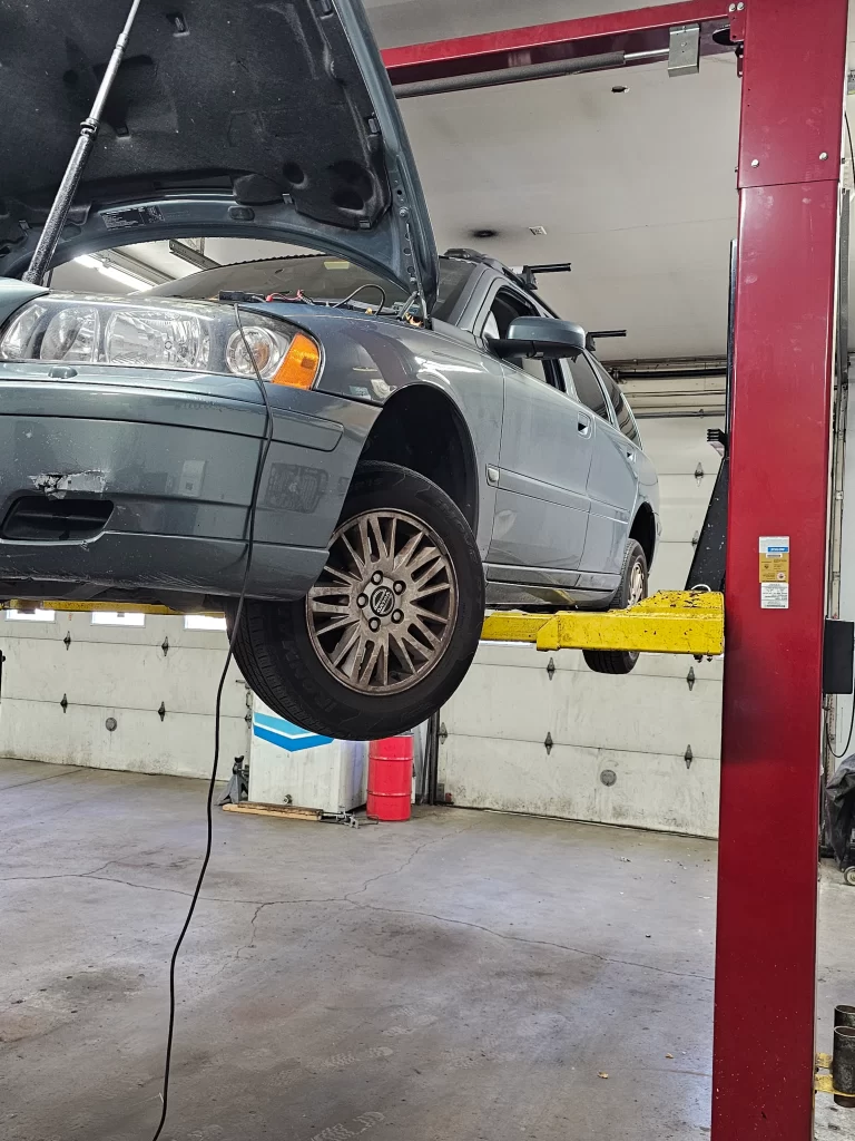 Car lifted on a hydraulic lift in an auto repair shop with the hood open for maintenance.