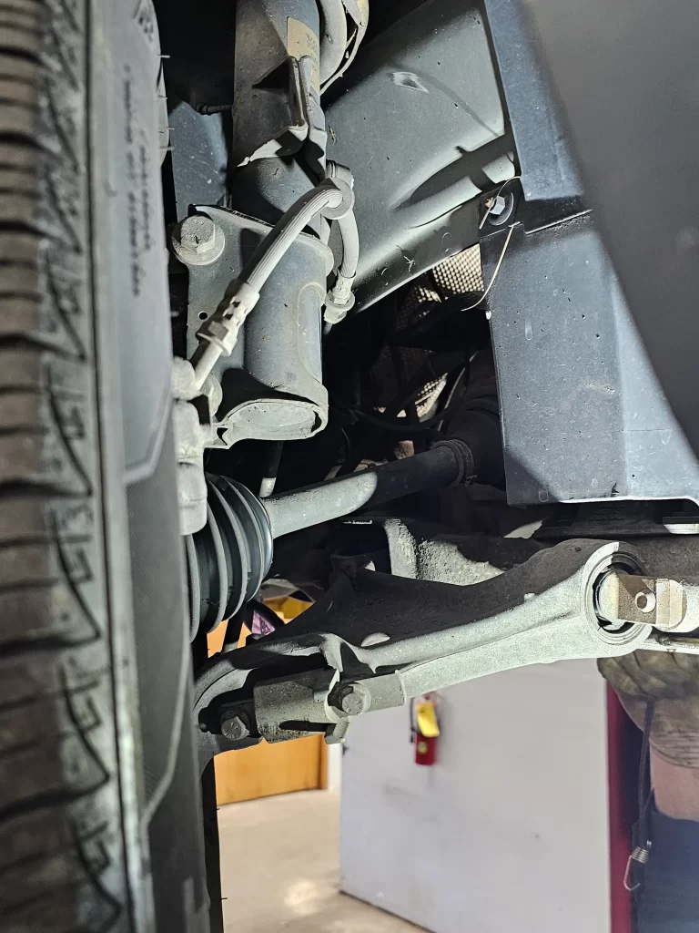 Close-up of a car's suspension system, including the control arm and brake line, on a lift.