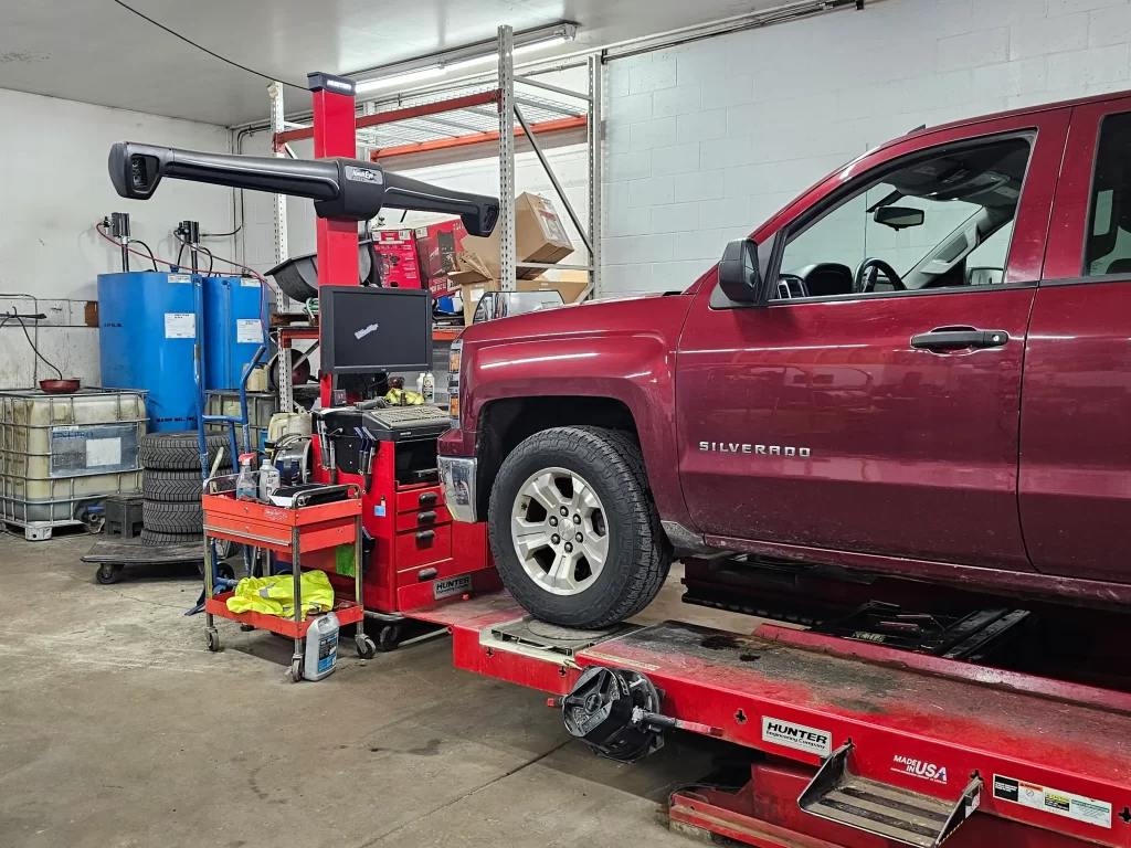 Red Chevrolet Silverado on a Hunter alignment rack in an auto repair shop.