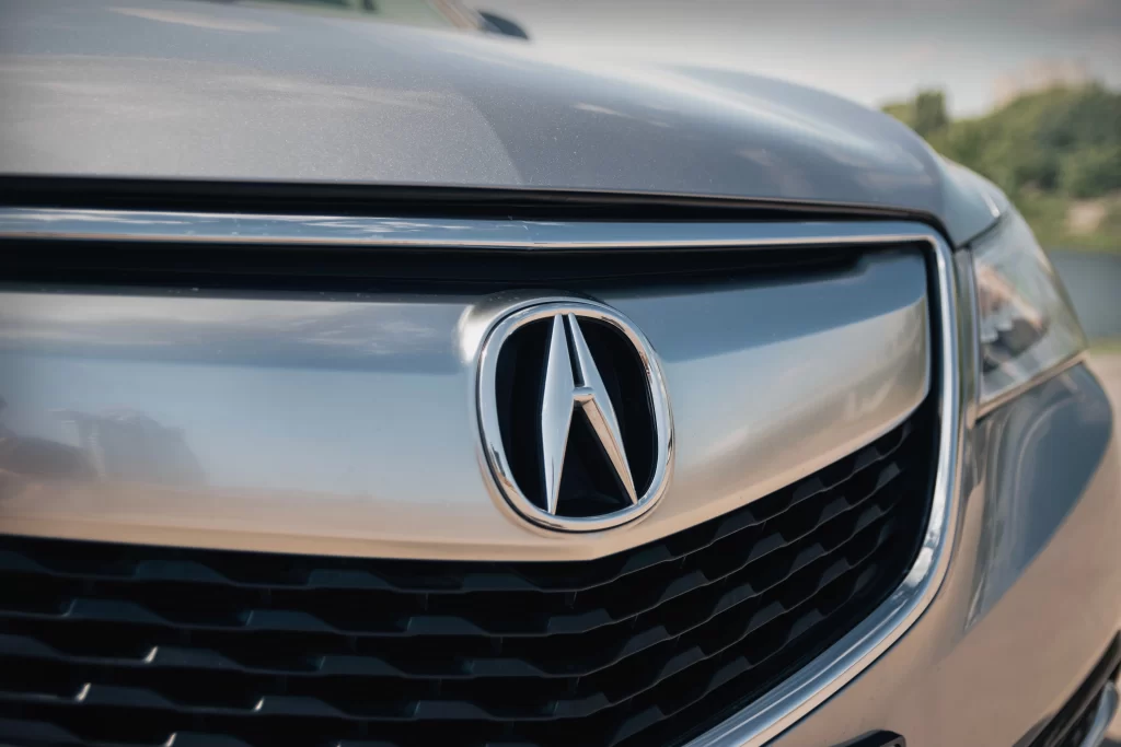 Close-up of an Acura car grille with the logo prominently displayed, reflecting light.