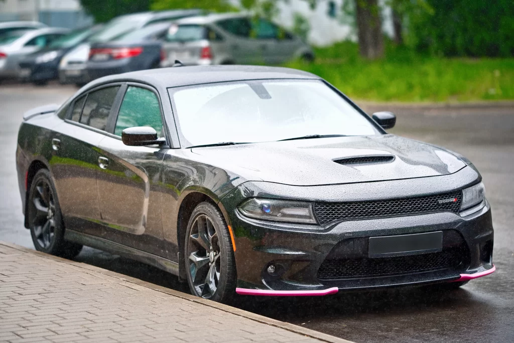 A black Dodge Charger sedan parked on a wet street, showcasing its sporty design and front grille.