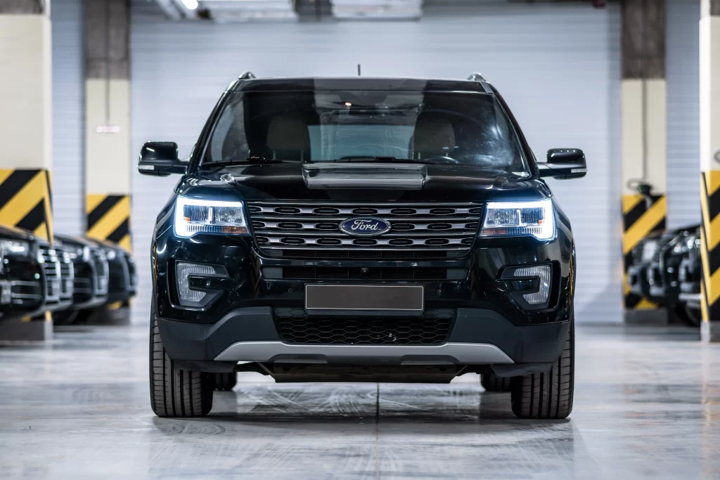 Front view of a black Ford SUV with headlights on, parked in an indoor garage.