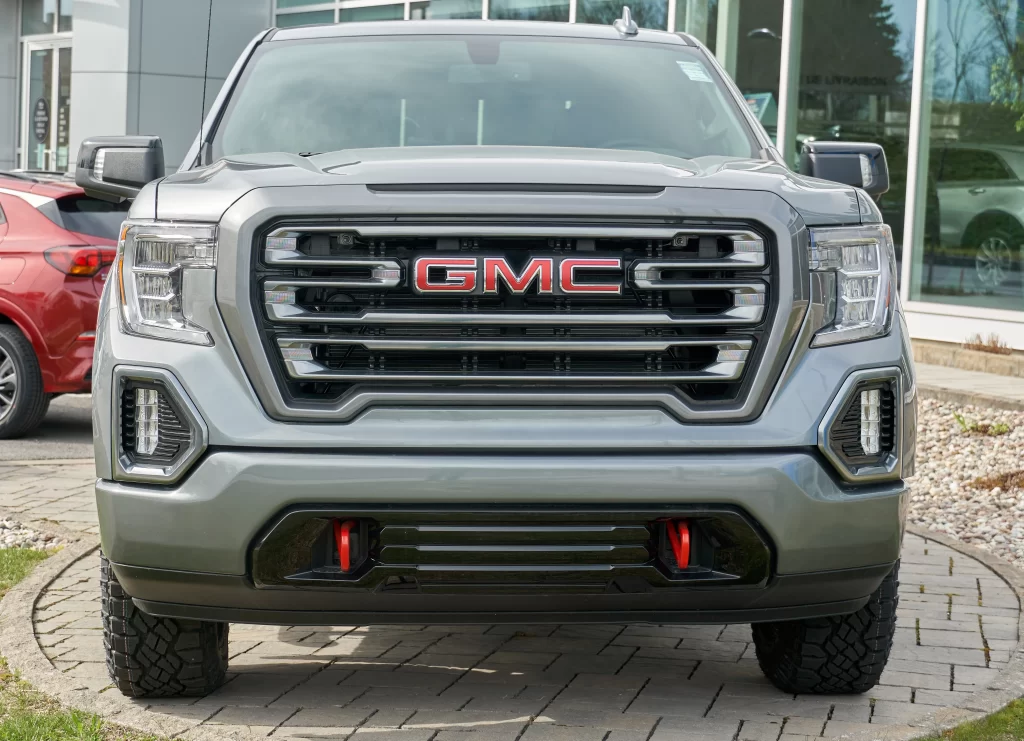 Front view of a gray GMC truck parked outside a dealership, featuring a bold grille and prominent GMC logo.