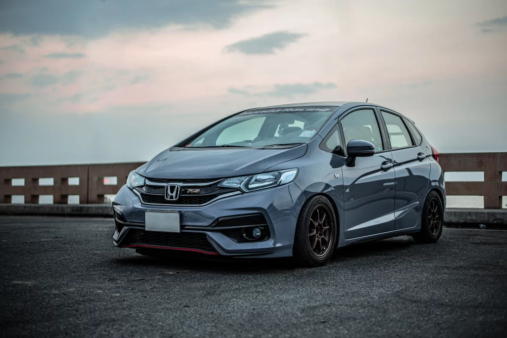 A gray Honda RS hatchback parked on a paved surface with a cloudy sky in the background.