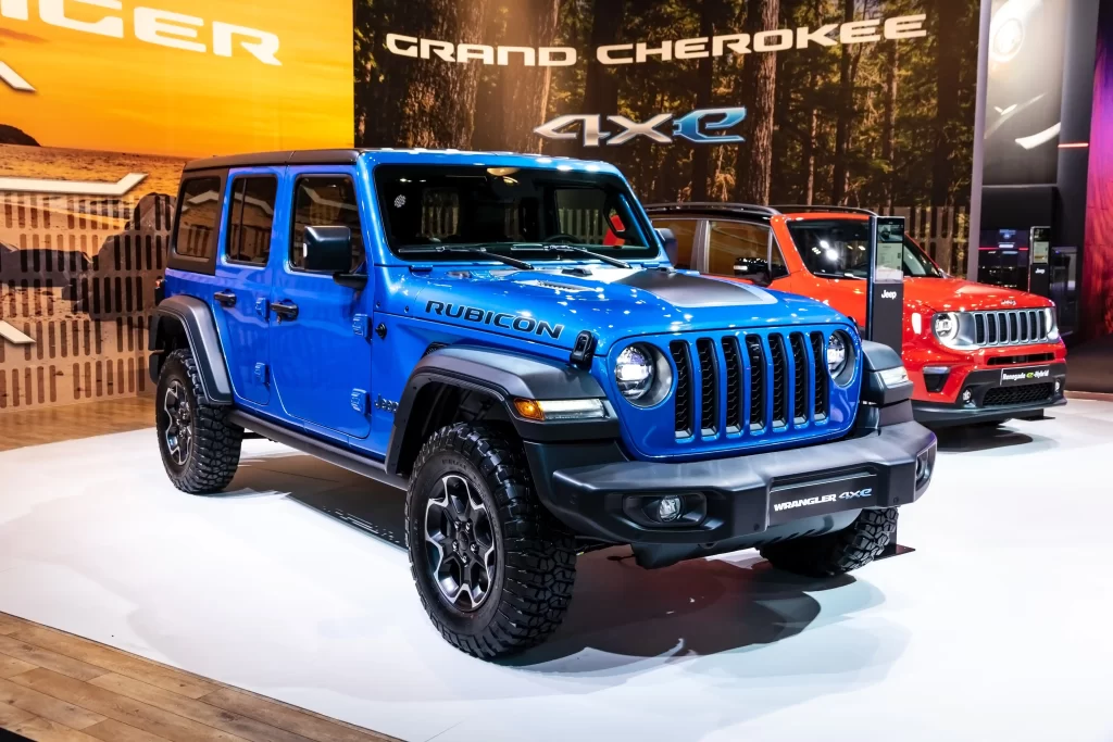 A blue Jeep Wrangler Rubicon 4xe displayed at an auto show, with other Jeep models in the background.