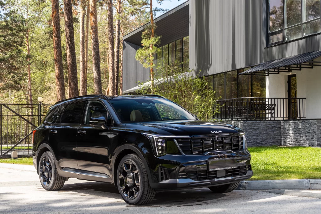 A sleek black Kia SUV parked in front of a modern building, surrounded by trees and greenery.