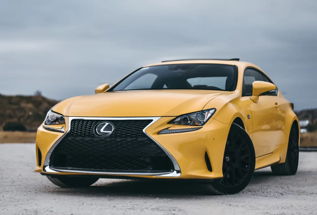 A yellow Lexus sports car parked outdoors under a cloudy sky, showcasing its sleek front design.