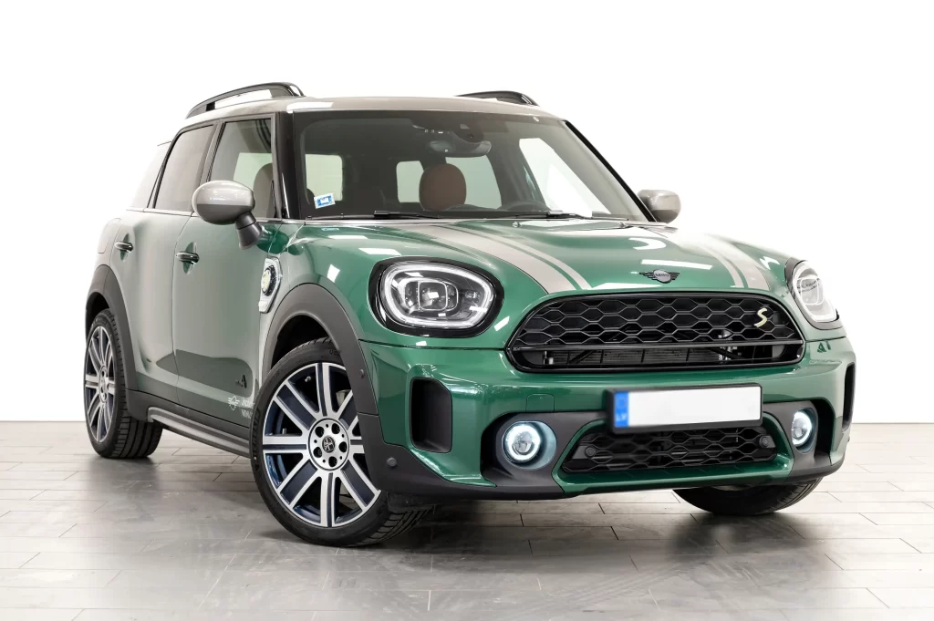 Green MINI Cooper with dual stripes, black grille, and distinct round headlights in a studio setting.