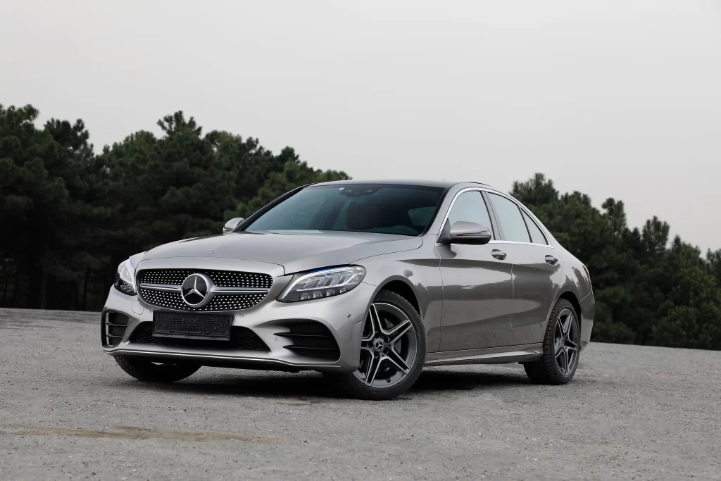 . Silver Mercedes-Benz sedan parked on gravel with trees in the background.