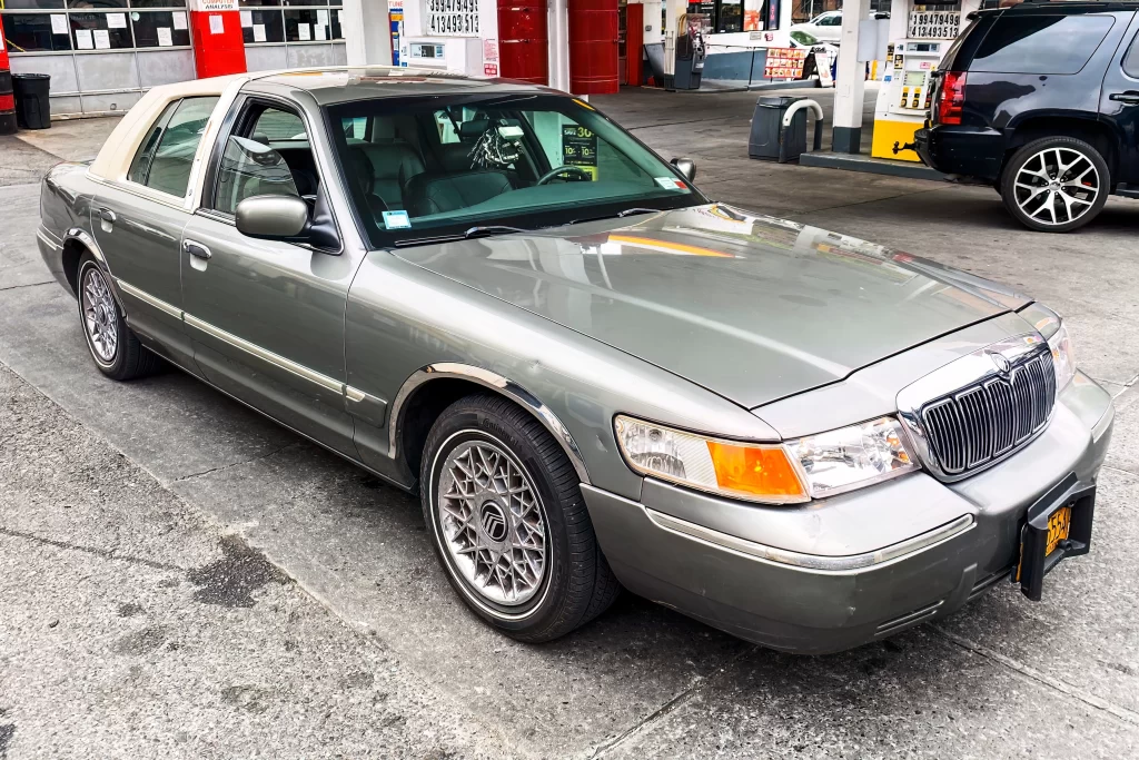 A gray Mercury Grand Marquis parked at a gas station with a beige vinyl roof and chrome accents.