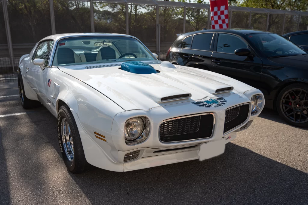 Classic white Pontiac Trans Am with hood scoop, blue Firebird decal, and dual front air intakes.