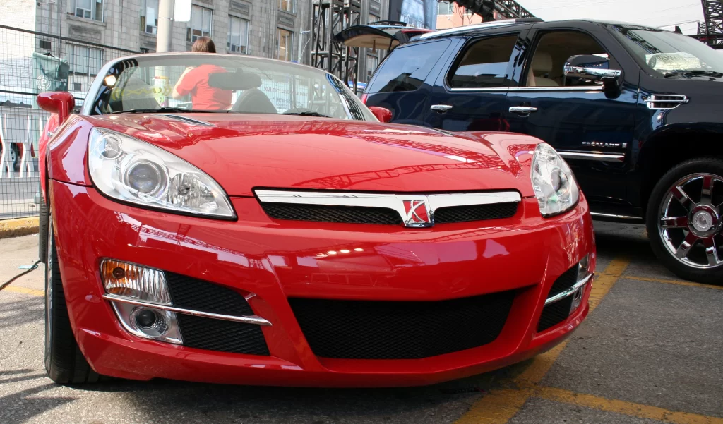 A red Saturn Sky convertible parked in an urban area, showcasing its sleek, sporty front design.