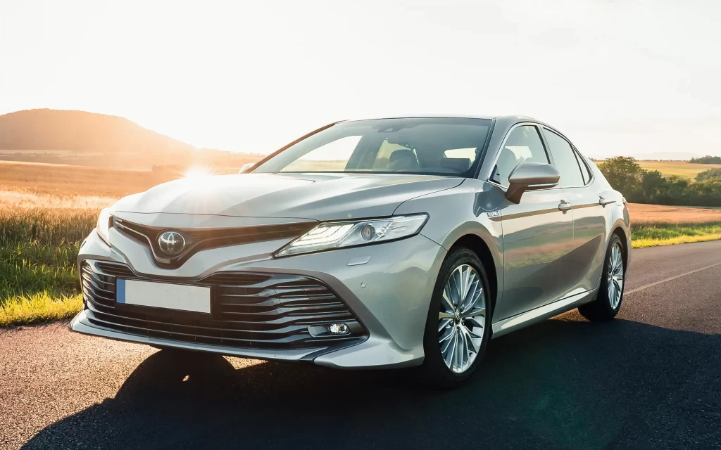 A silver Toyota sedan parked on a road at sunset, with a sleek design and prominent front grille.