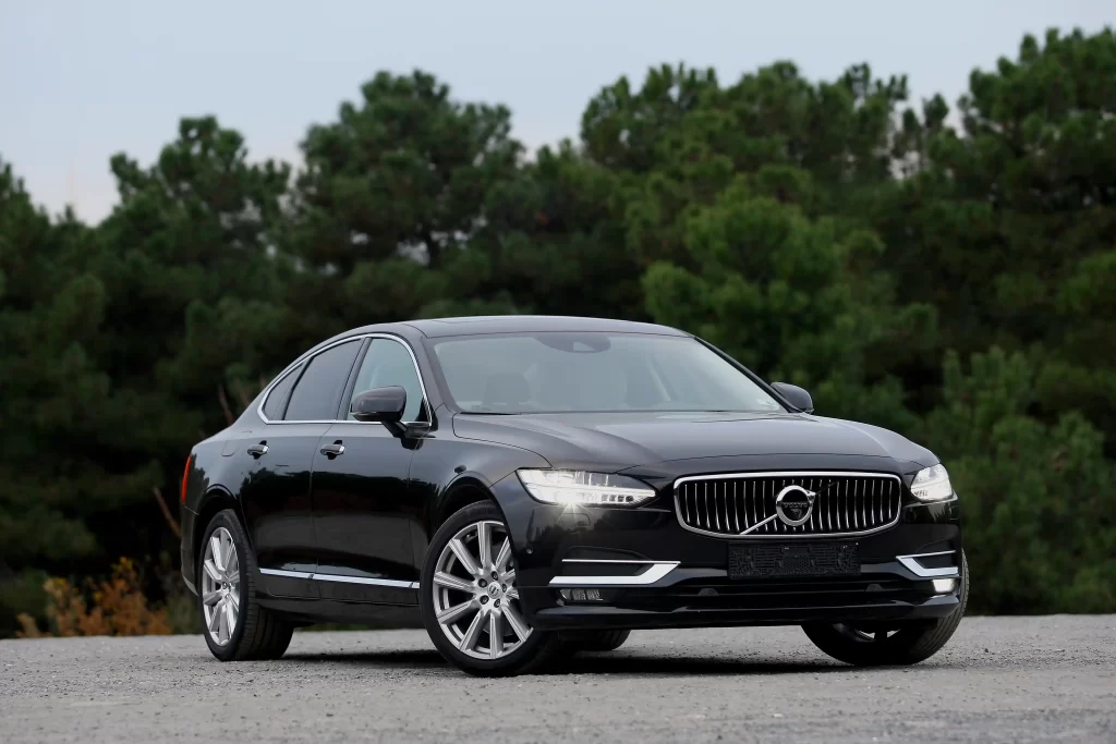 Black Volvo S90 sedan parked outdoors with trees in the background.