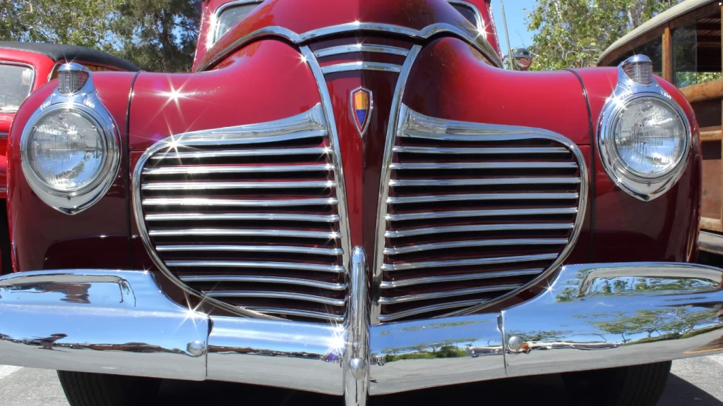 Close-up of a vintage red Plymouth car front, showcasing its chrome grille and classic round headlights.